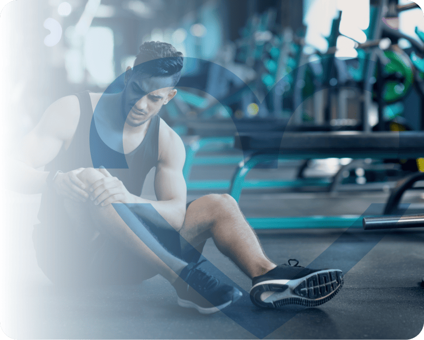 Hombre joven con ropa deportiva sentado en gimnasio sosteniendo su rodilla lesionada
