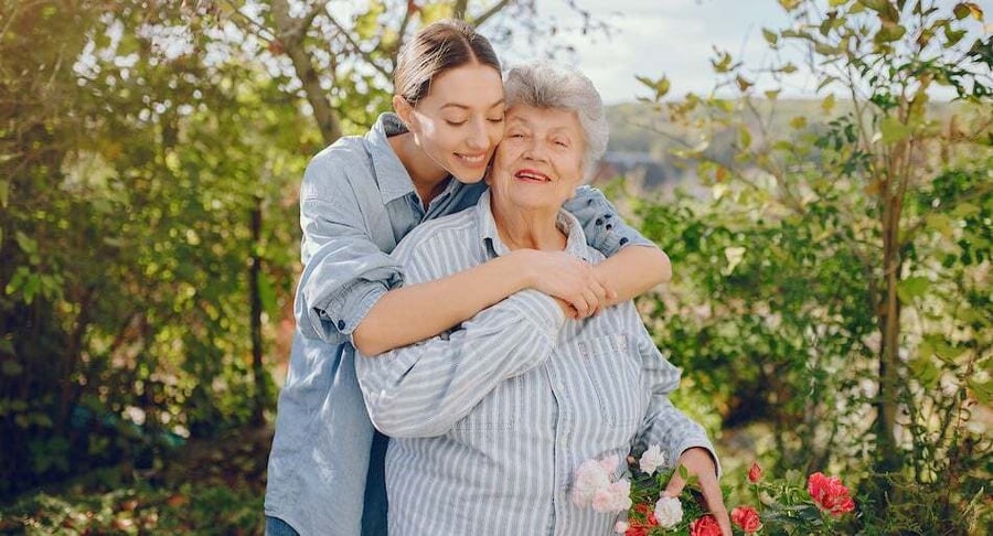 Young woman lovingly embracing an older adult in a flower garden