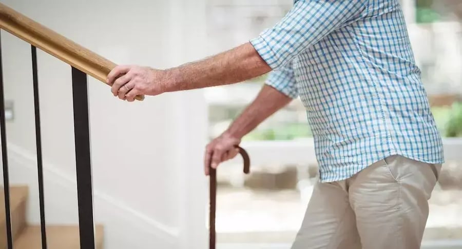 Older adult climbing stairs with cane and handrail support