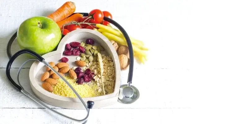 Healthy food in heart-shaped container next to a stethoscope for heart care
