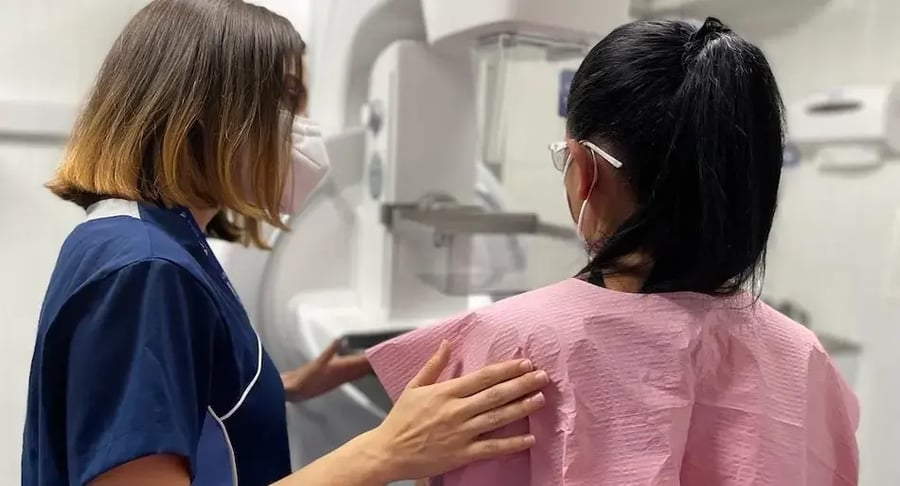 Técnica médica asiste a una paciente durante la colocación para un examen de mamografía.