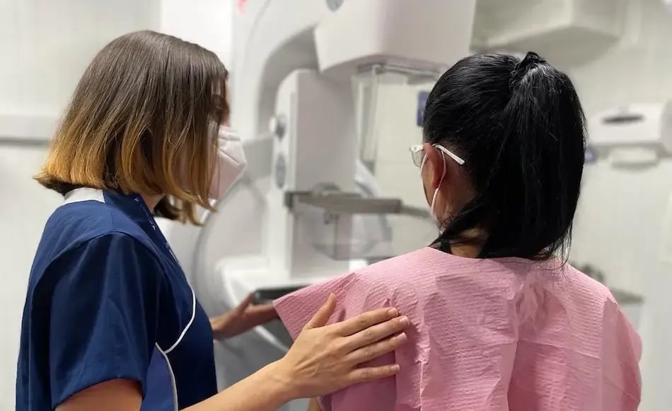 Profesional de salud asistiendo a una paciente durante el proceso de colocación en un mamógrafo dentro de la sala médica.