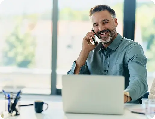 Un hombre sonriente atiende una llamada telefónica mientras trabaja frente a su computadora portátil.