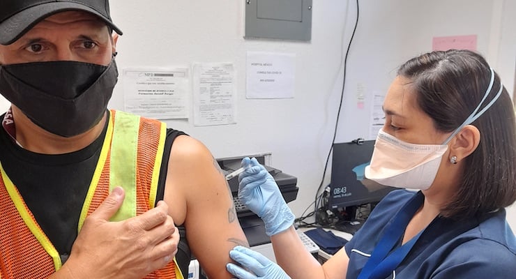 Una enfermera del Hospital Clínica Bíblica con mascarilla aplica la vacuna contra la influenza a un hombre con chaleco de seguridad en un centro penal.