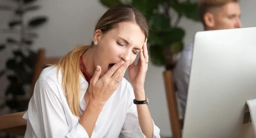 Tired woman in office yawning in front of computer due to work fatigue