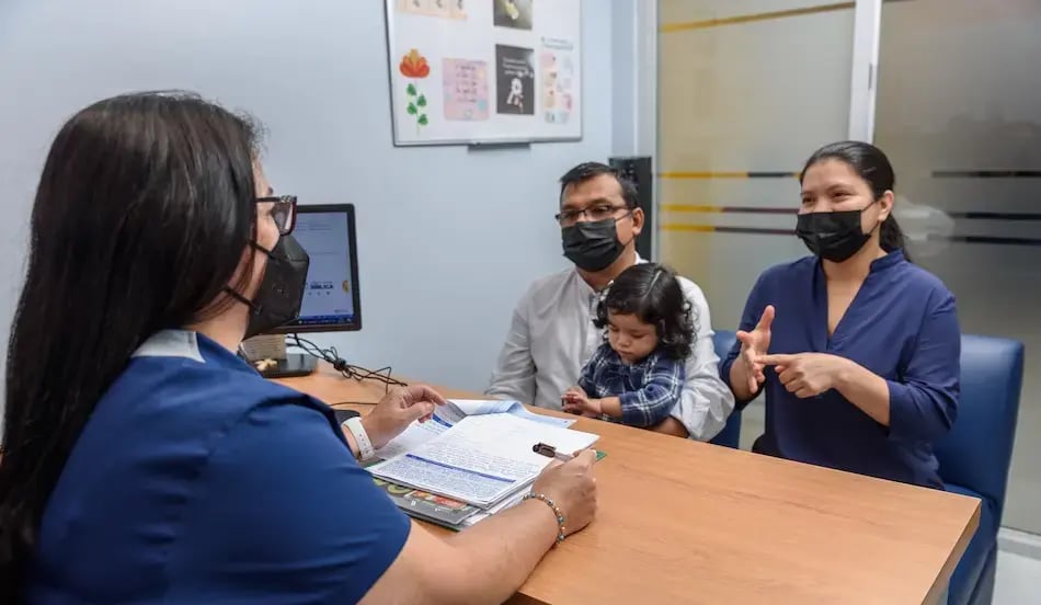 Profesional de salud atendiendo a una familia con una niña pequeña durante una consulta en oficina médica.