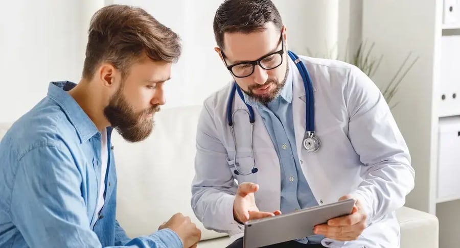 Médico mostrando información en una tableta a un paciente sentado durante una consulta.