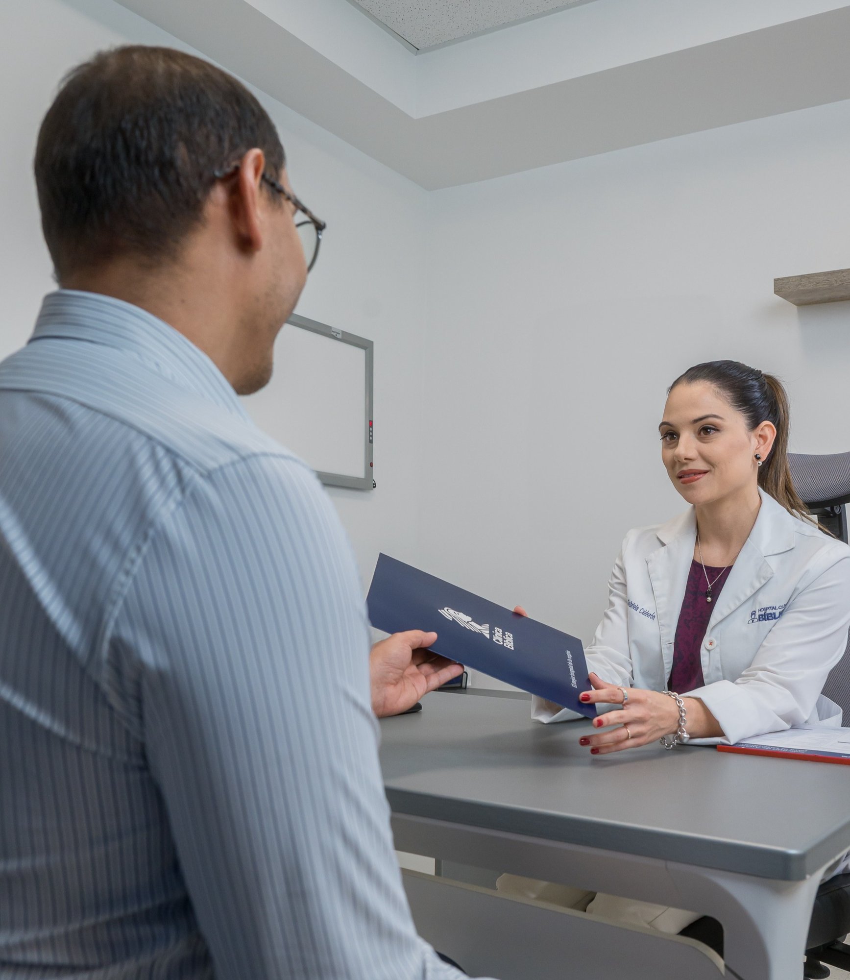 Doctora entregando un folleto informativo de la Clínica Bíblica a un paciente durante una consulta médica.