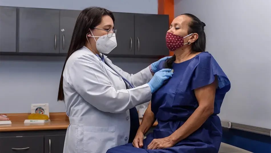 Doctora revisando a una paciente con bata azul durante una consulta médica en el hospital.
