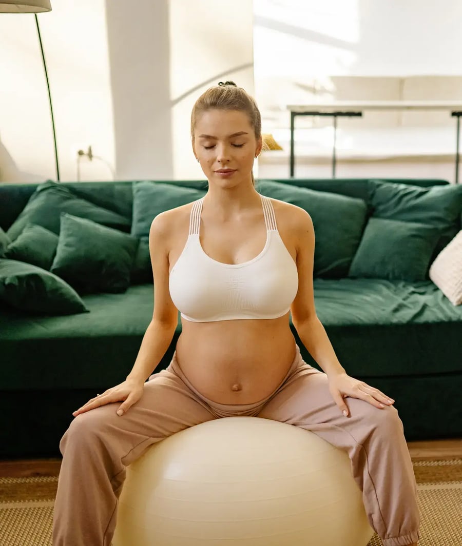 Pregnant woman doing prenatal exercises on a pilates ball at home.