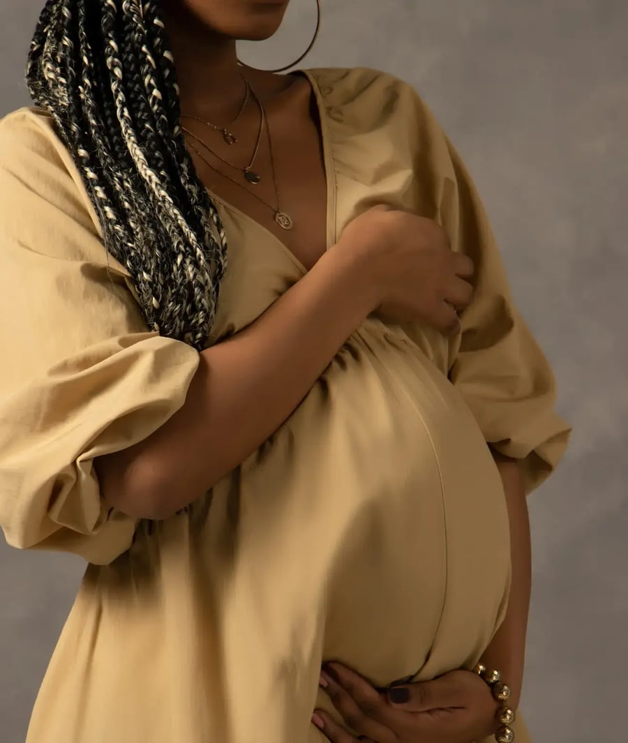 Pregnant woman in beige dress caressing her belly at the Clinica Biblica.