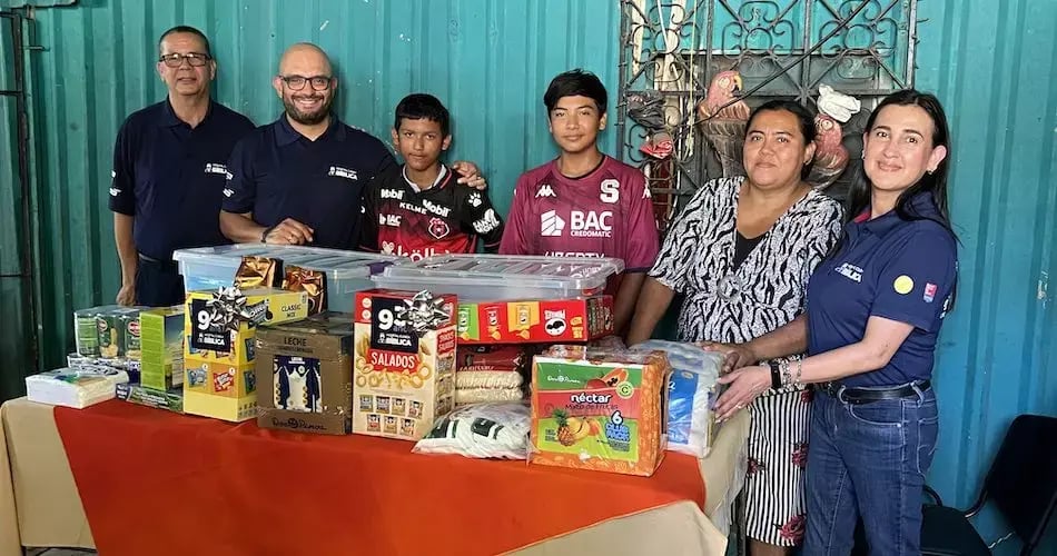 Grupo de personas entregando víveres y productos a una familia frente a una mesa con alimentos.
