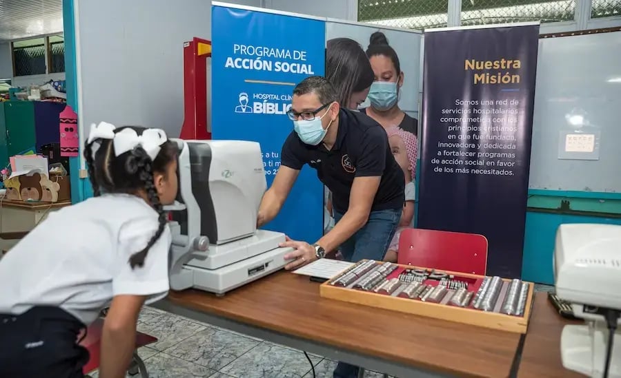 Profesional realizando un examen de visión a una niña con equipo óptico en un aula escolar.