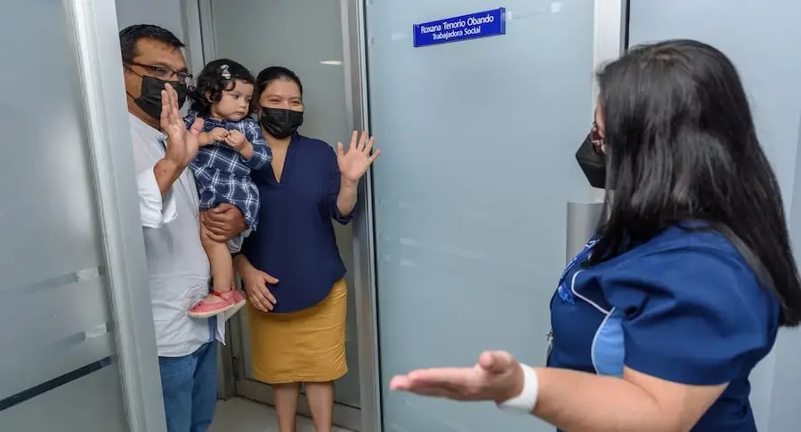 Familia con niña pequeña saludando a una profesional de salud en la entrada de una oficina médica.
