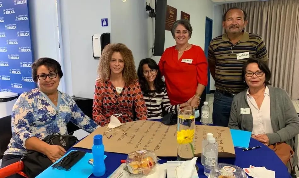 Grupo de seis personas posando alrededor de una mesa con una cartulina con notas durante una actividad grupal.