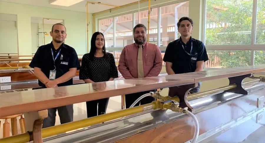 Cuatro personas de pie en un laboratorio con mesas y equipo hidráulico.