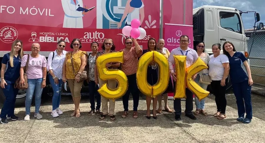 Grupo de personas frente a una unidad móvil de salud sosteniendo globos dorados con la cifra 50K.