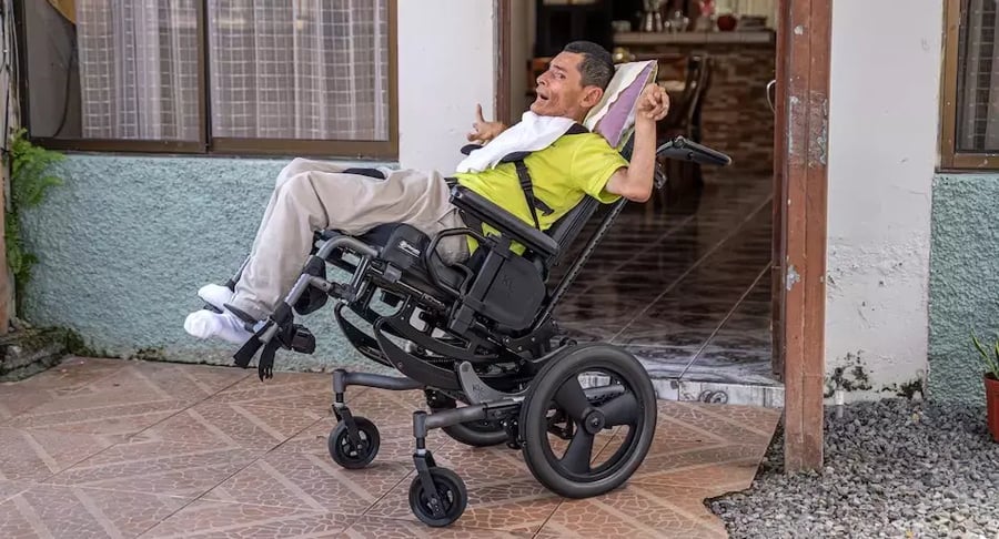 Hombre sentado en una silla de ruedas reclinable en la entrada de una casa.