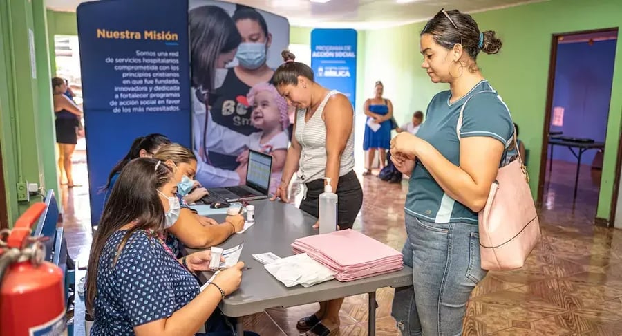 Personas registrándose en una mesa de atención durante una actividad comunitaria con personal revisando documentos y equipos en el lugar.