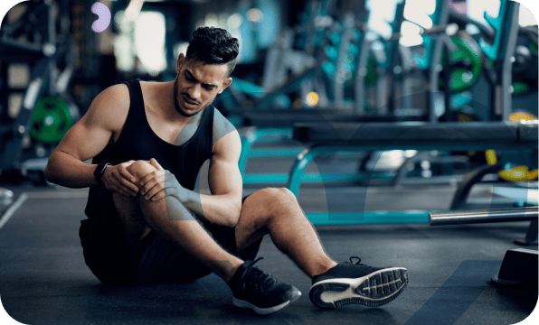 Hombre joven con ropa deportiva sentado en gimnasio sosteniendo su rodilla lesionada