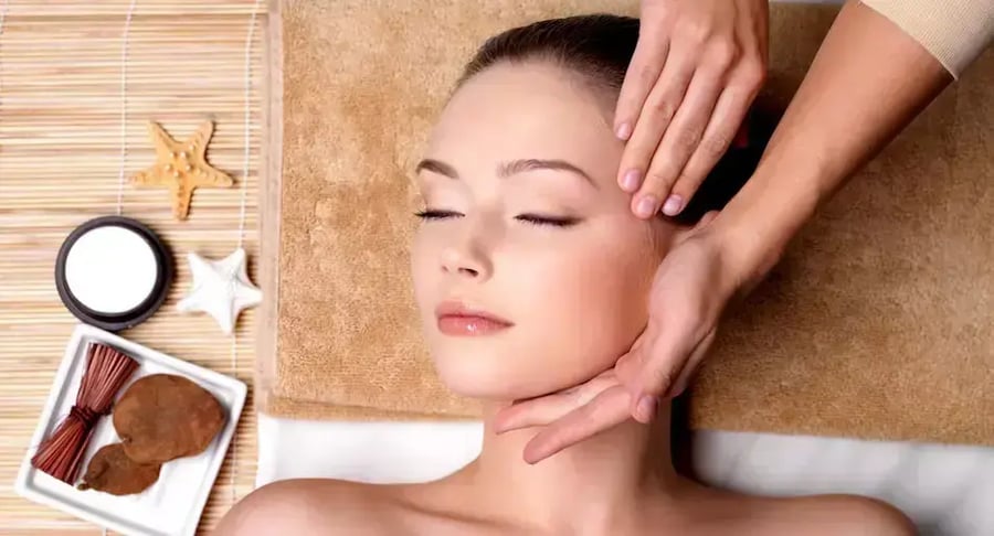Woman receiving relaxing facial massage at spa with skin care products