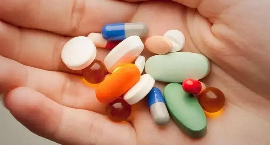 Hand holding different pills and medicine capsules of various colors.