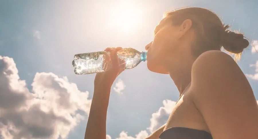 Young woman hydrating herself with bottled water in the sun to take care of her health.