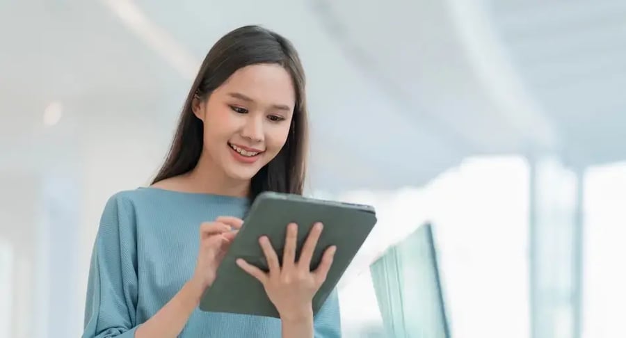 Mujer joven sonriendo mientras utiliza una tablet en un espacio interior luminoso.