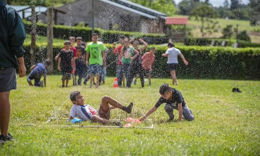 Niños deslizándose y jugando bajo un rociador de agua en un área de césped.