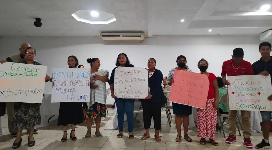 Personas alineadas sosteniendo carteles de agradecimiento en un salón.