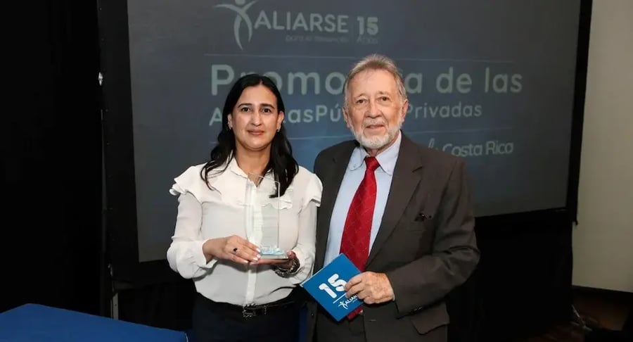 Mujer recibiendo un reconocimiento junto a un hombre en un evento de Aliarse.