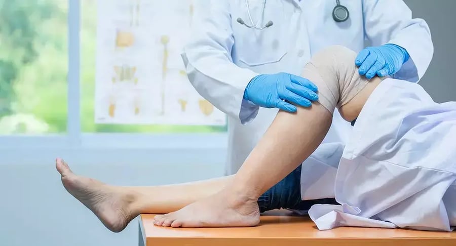 Physician checking the bandaged knee of a patient undergoing rehabilitation.