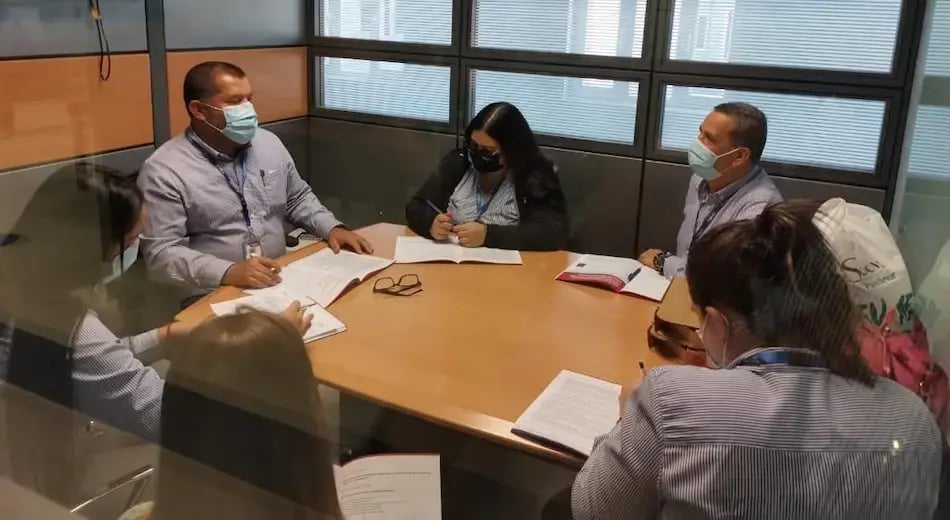 Personas con mascarilla reunidas en una mesa tomando notas durante una sesión de trabajo.