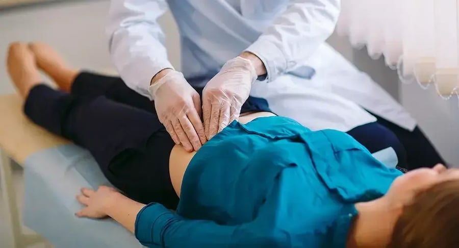 Physician examining the abdomen of a patient lying on a stretcher.
