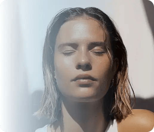 Rostro de mujer joven con ojos cerrados disfrutando del sol, piel saludable y luminosa