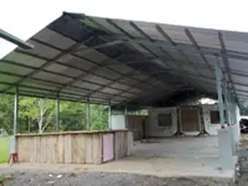 Estructura techada abierta con paredes de madera y piso de concreto en un entorno rural.
