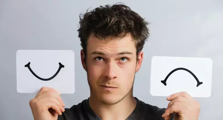 Young man holding happy and sad face cards as a symbol of mental health