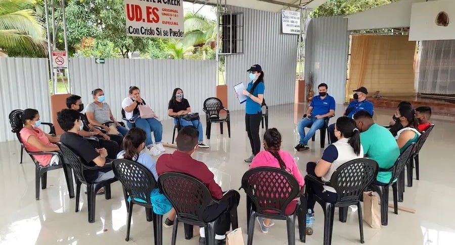 Persona facilitadora dando una charla a un grupo de jóvenes sentados en círculo en un salón abierto.