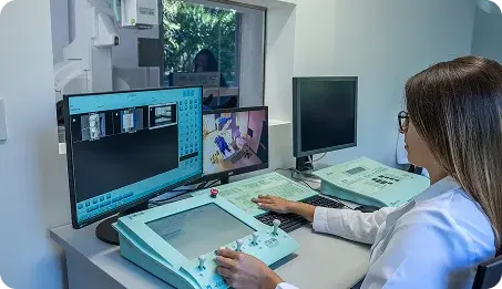 Una especialista de salud opera una consola con monitores de diagnóstico por imágenes médicas en una sala de control.