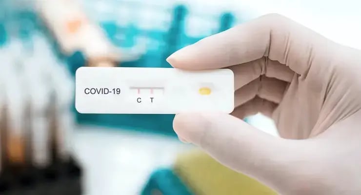 Gloved hand holding a rapid antigen test for COVID-19 with the letters C and T visible.