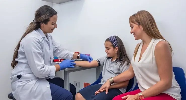 Doctor taking blood sample from a girl in the company of her mother in the doctor's office