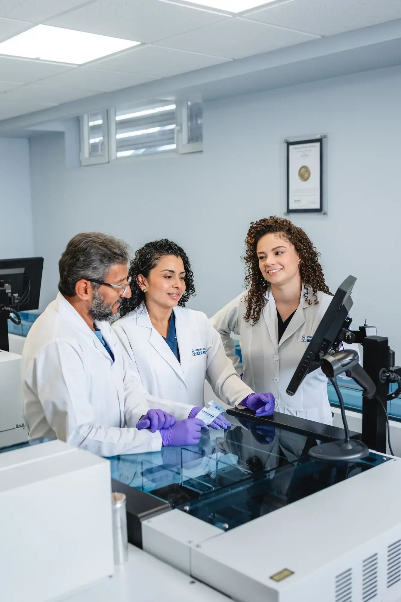 Tres médicos en laboratorio con bata blanca revisando muestras en un monitor