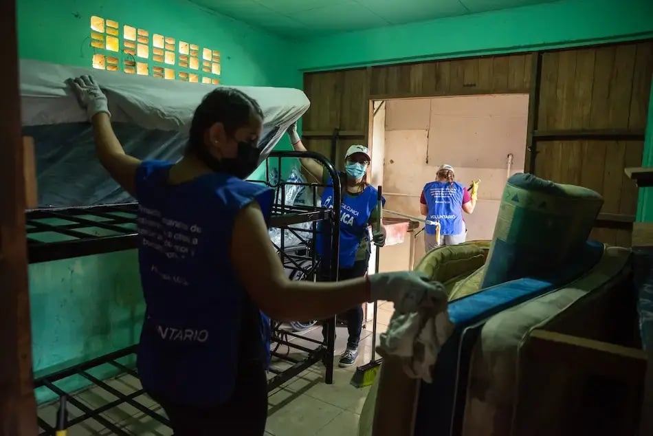 Voluntarias acomodando literas y colchones dentro de una habitación mientras realizan labores de limpieza.