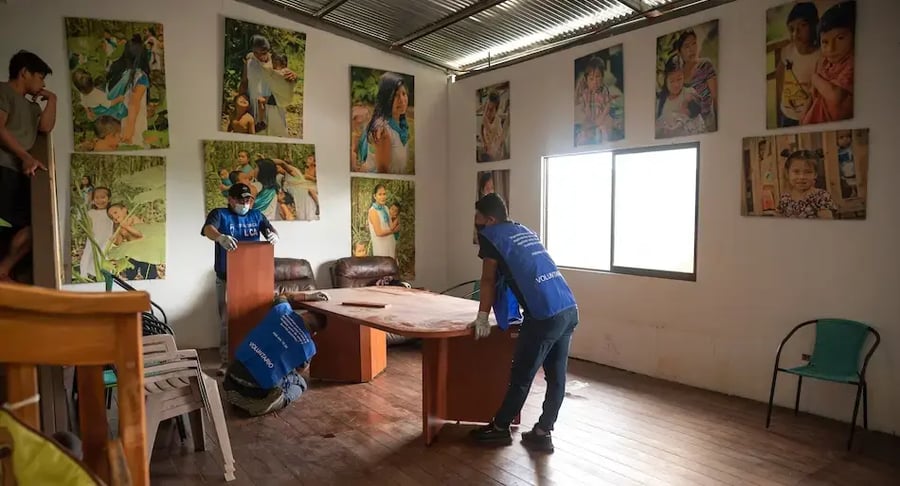 Grupo de voluntarios moviendo muebles dentro de una sala decorada con fotografías de niños.
