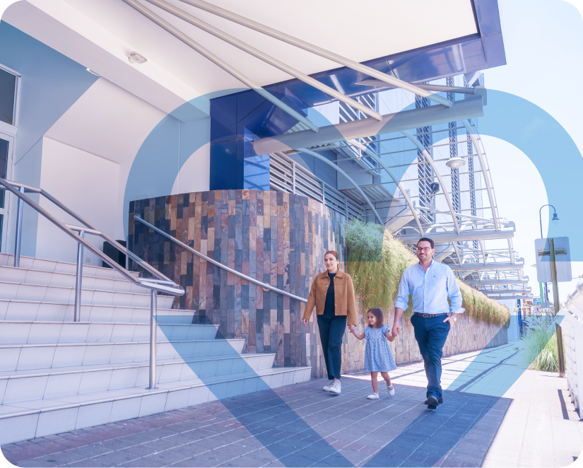 Familia caminando tomada de la mano frente a la entrada principal de Clínica Bíblica.
