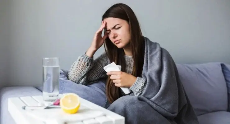 Sick woman at home with fever and headache covered with blanket