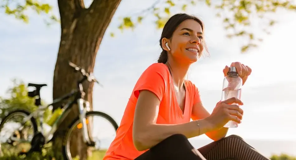 Sportswoman resting outdoors with bicycle and hydrating with water